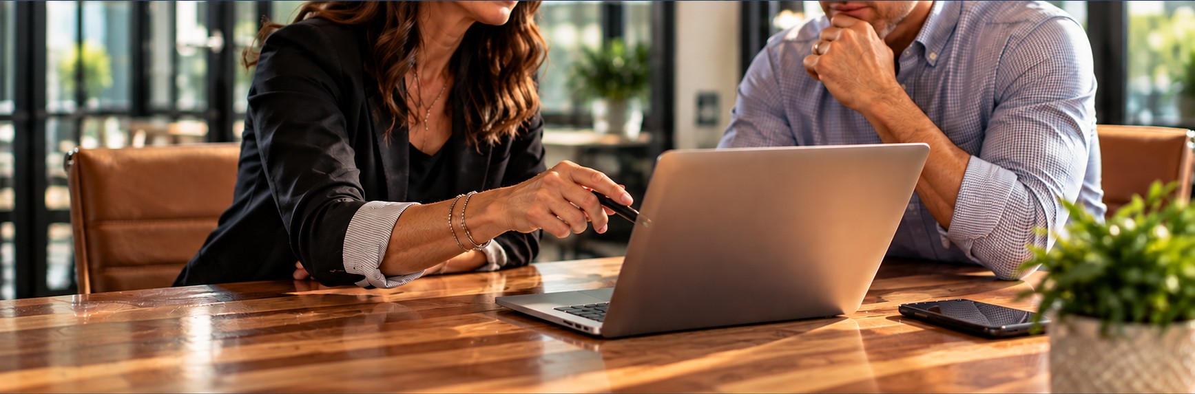 Two professionals collaborating at a laptop across a sunlit conference table